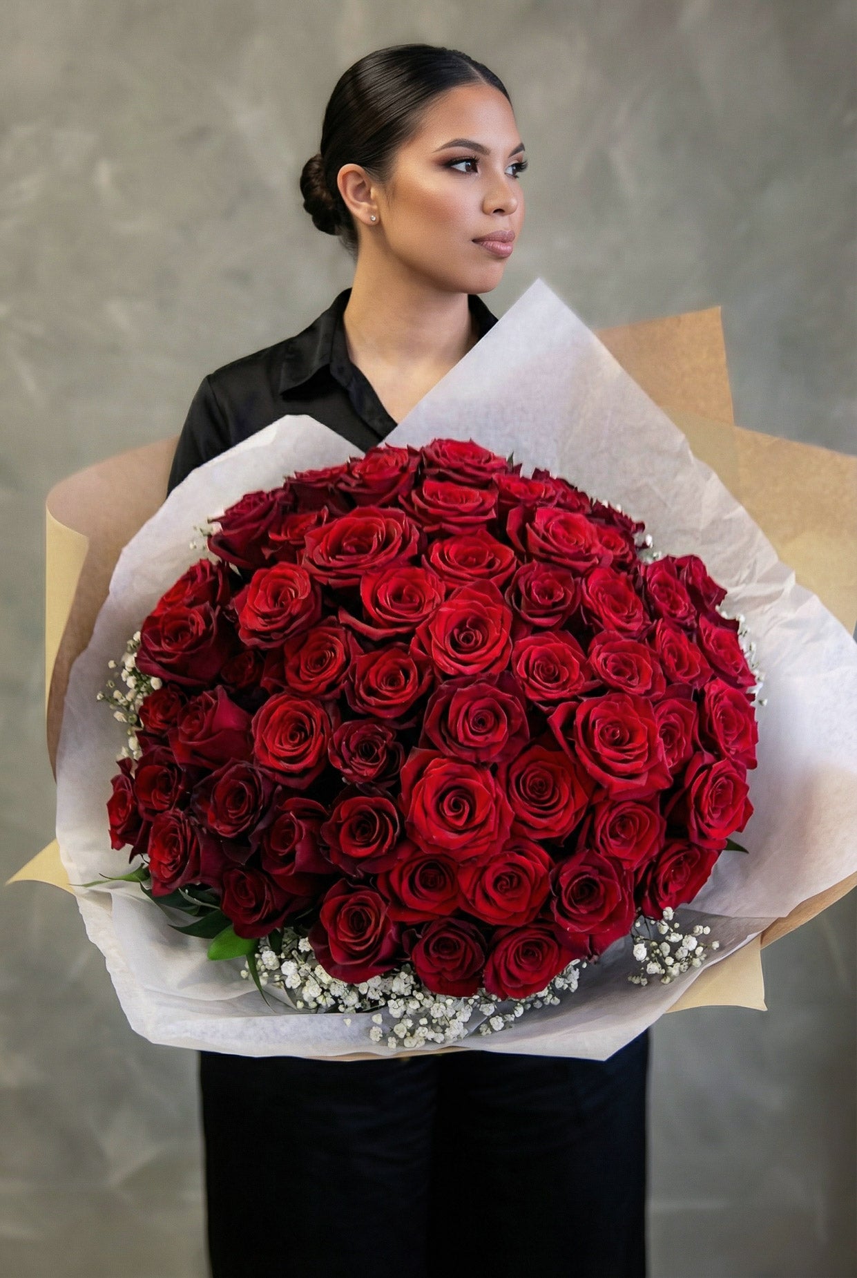 Woman holding a bouquet of 50 red roses against a neutral background
