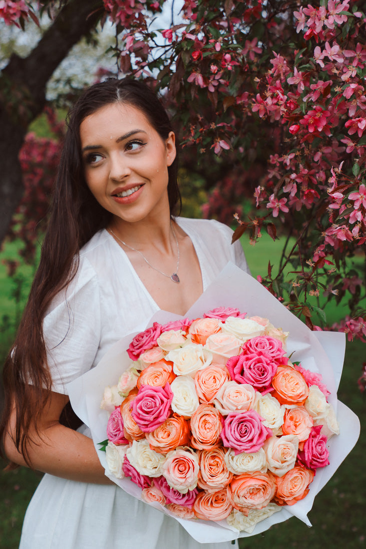 A large bouquet of 50 spring-toned roses in pink, peach, and white, lush and romantic
