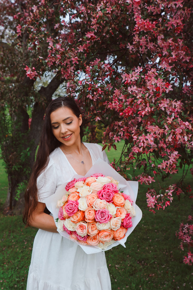 A large bouquet of 50 spring-toned roses in pink, peach, and white, lush and romantic