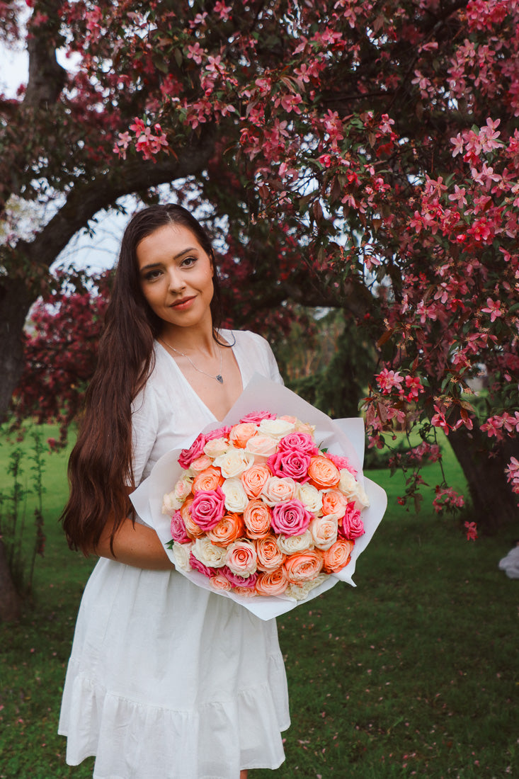 A large bouquet of 50 spring-toned roses in pink, peach, and white, lush and romantic