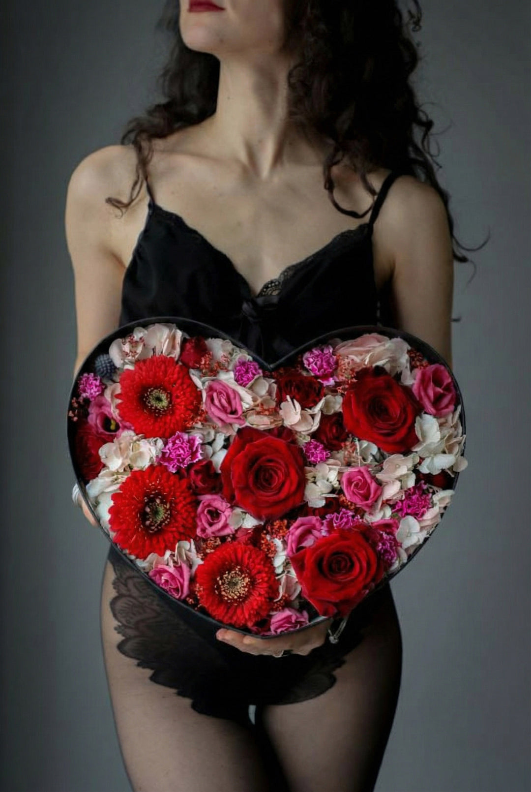 Woman holding a heart-shaped box of flowers against a gray background