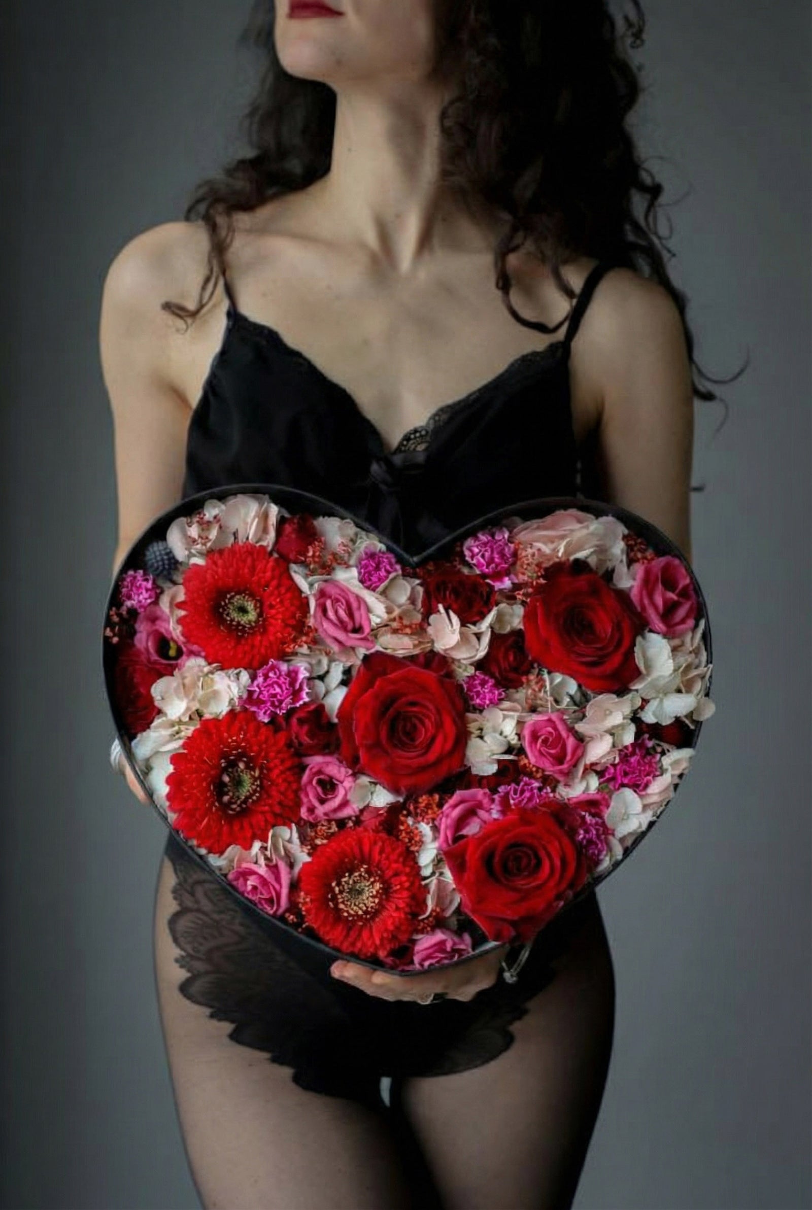 Woman holding a heart-shaped box of flowers against a gray background
