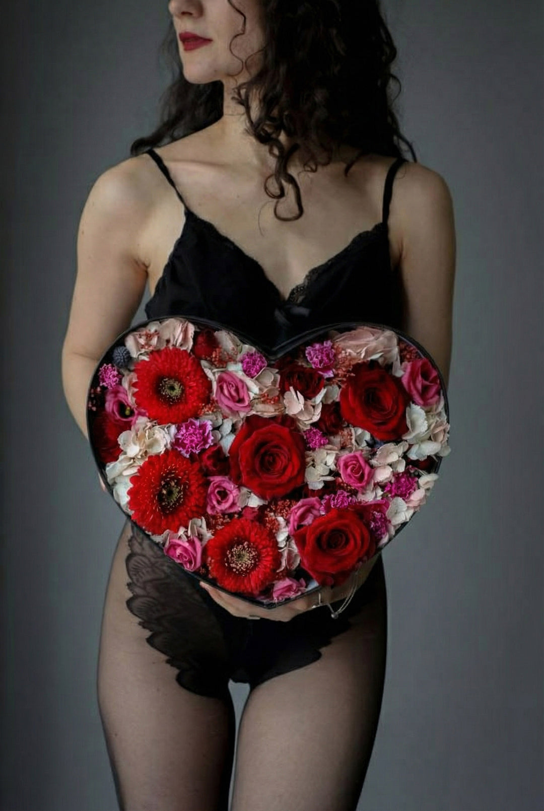 Woman holding a heart-shaped box of flowers against a gray background