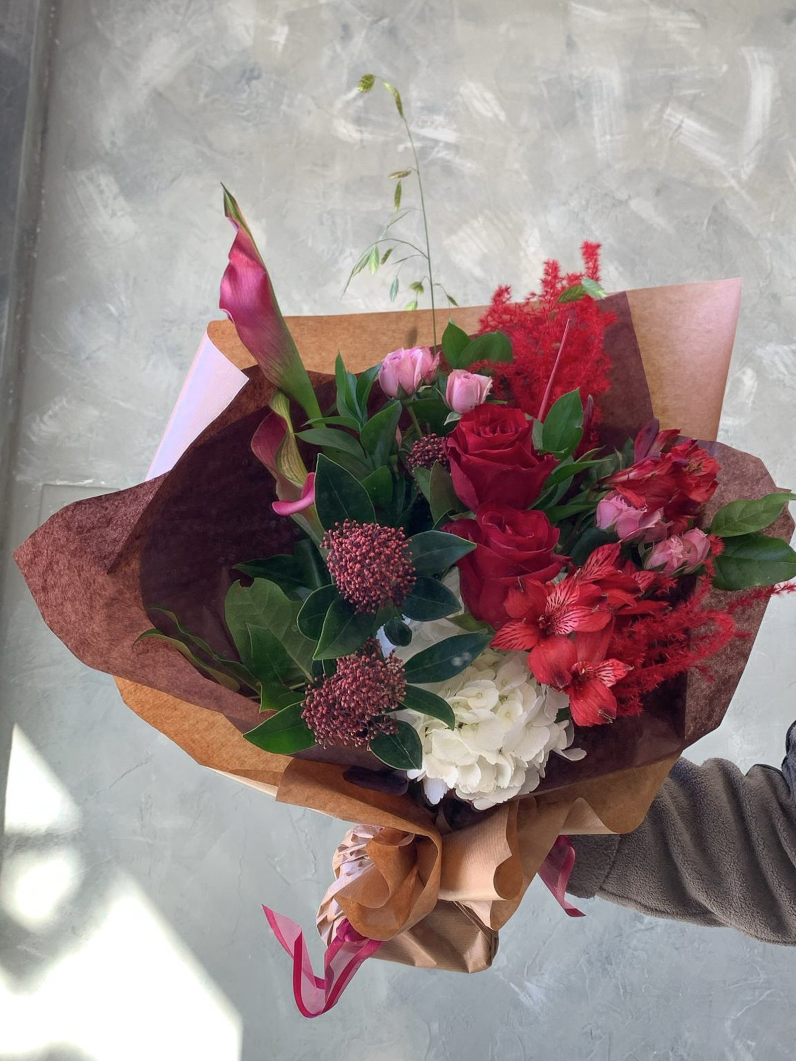 Bouquet of red, pink, white  flowers wrapped in brown paper against a light background