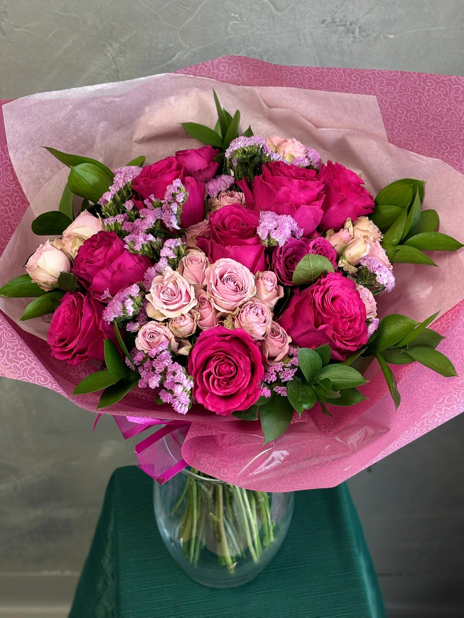 Bouquet of pink and white roses in a clear vase on a green surface with a pink paper wrap.