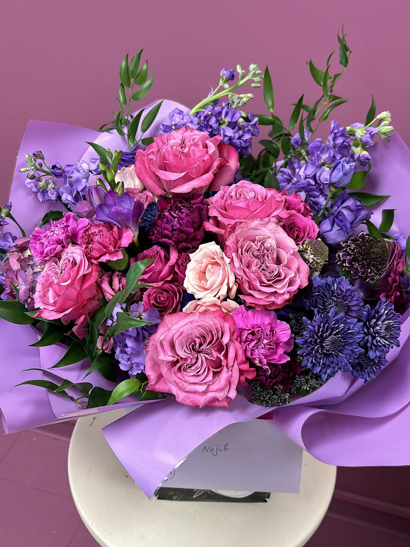 Bouquet of pink, blue and purple flowers with green leaves on a pink background