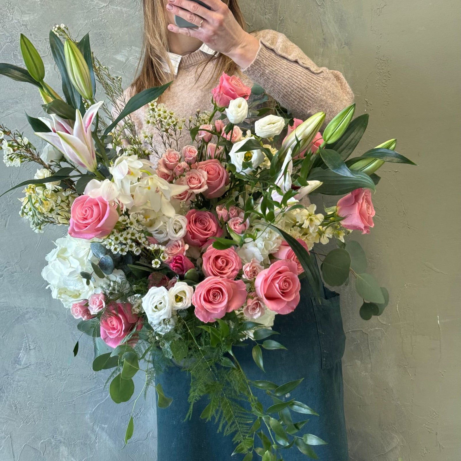 Person holding a large bouquet of flowers with pink and white roses against a neutral background