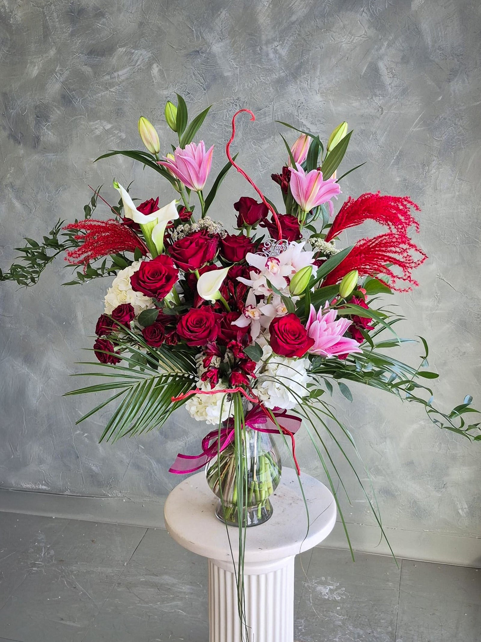 Bouquet of red, pink, and white flowers with greenery in a clear vase on a gray background