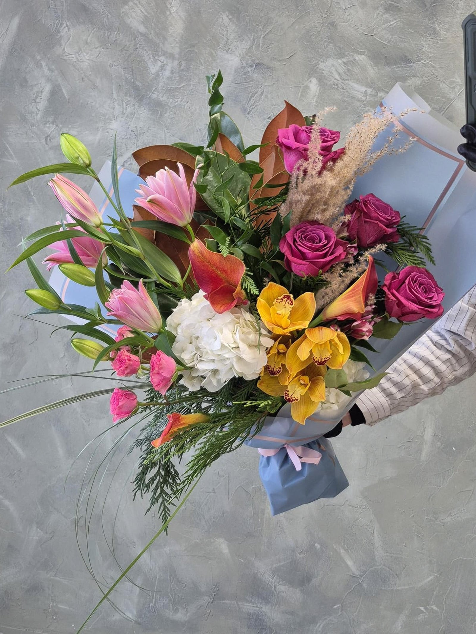 colorful bouquet with bright summer flowers - yellow cymbidium orchids, mauve roses, pink lilies and orange calla lilies