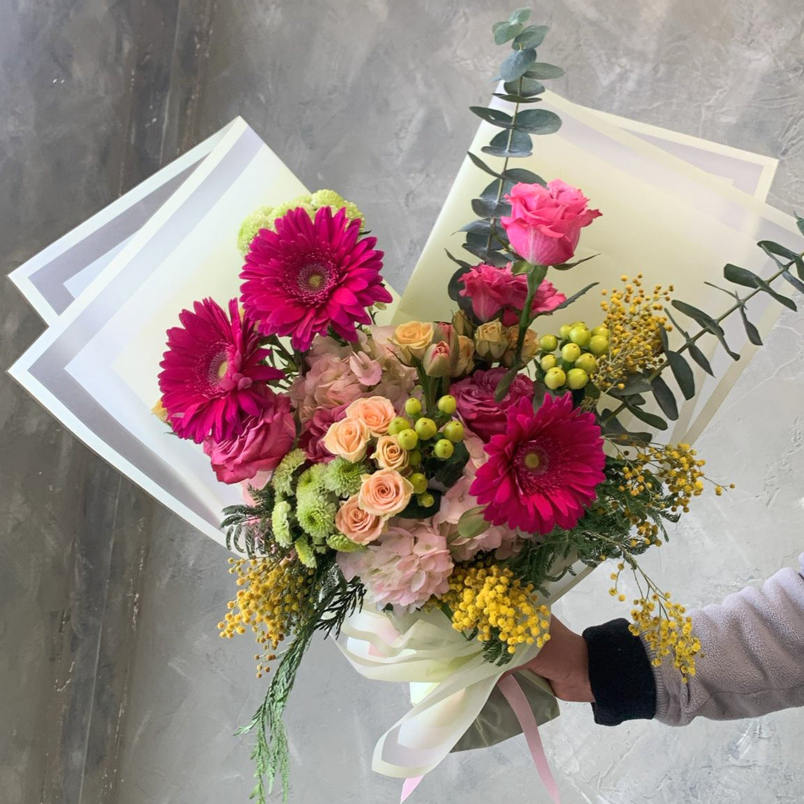 Bouquet of colorful flowers held by a person against a gray background