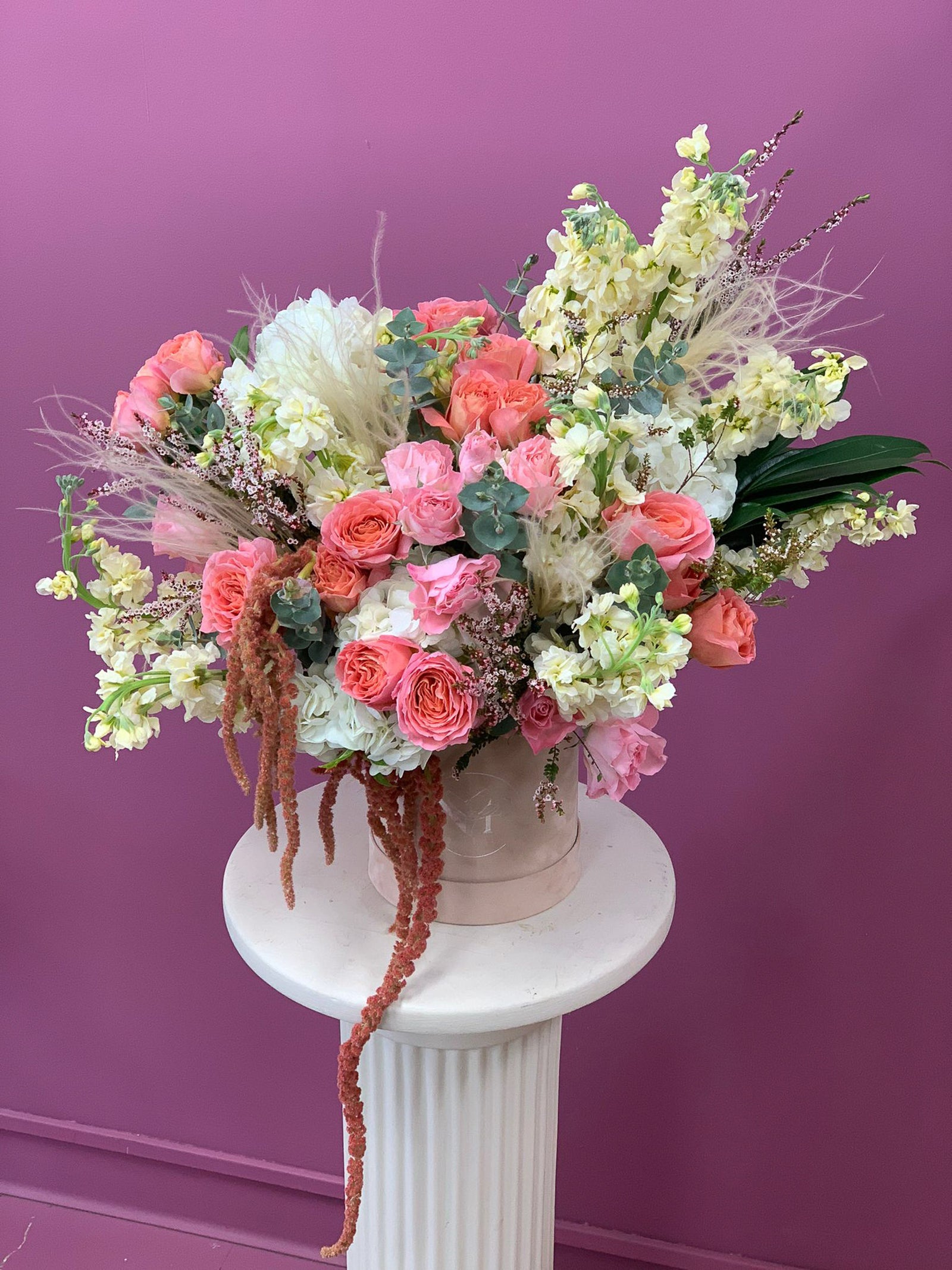 Bouquet of bright flowers in a velvet box on a white pedestal against a purple background