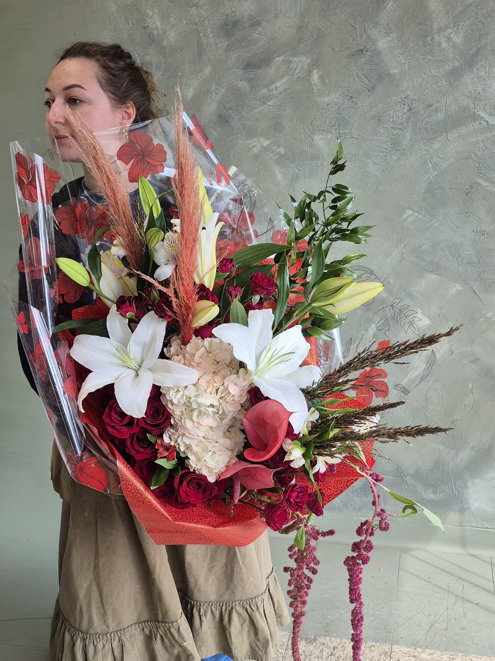 Person holding a large bouquet of white and red flowers against a plain background