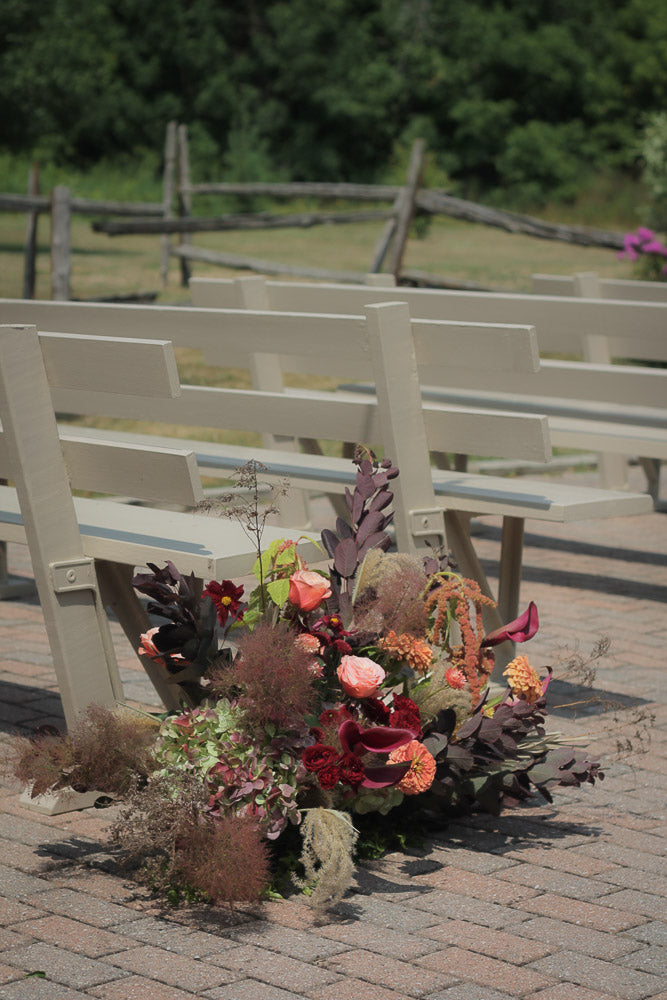 Decorative floral arrangement with autumnal elements on a bench outdoors.