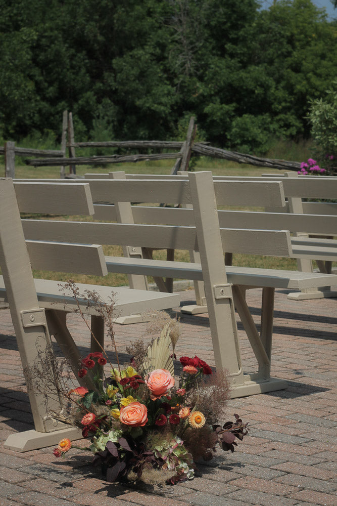 Decorative floral arrangement on a stone pathway with wooden chairs in the background.
