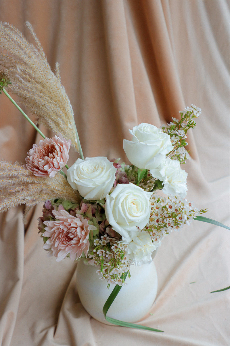 Silk & Earth elegant ivory flower arrangement with white roses and cream florals in light ceramic vase.
