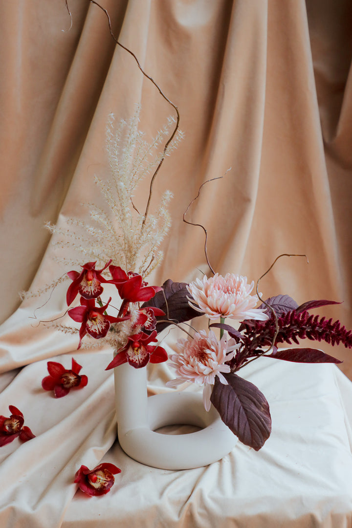 Ember Grace small fall centerpiece in ivory ceramic vase with two openings, featuring burgundy, peach, and ivory flowers.