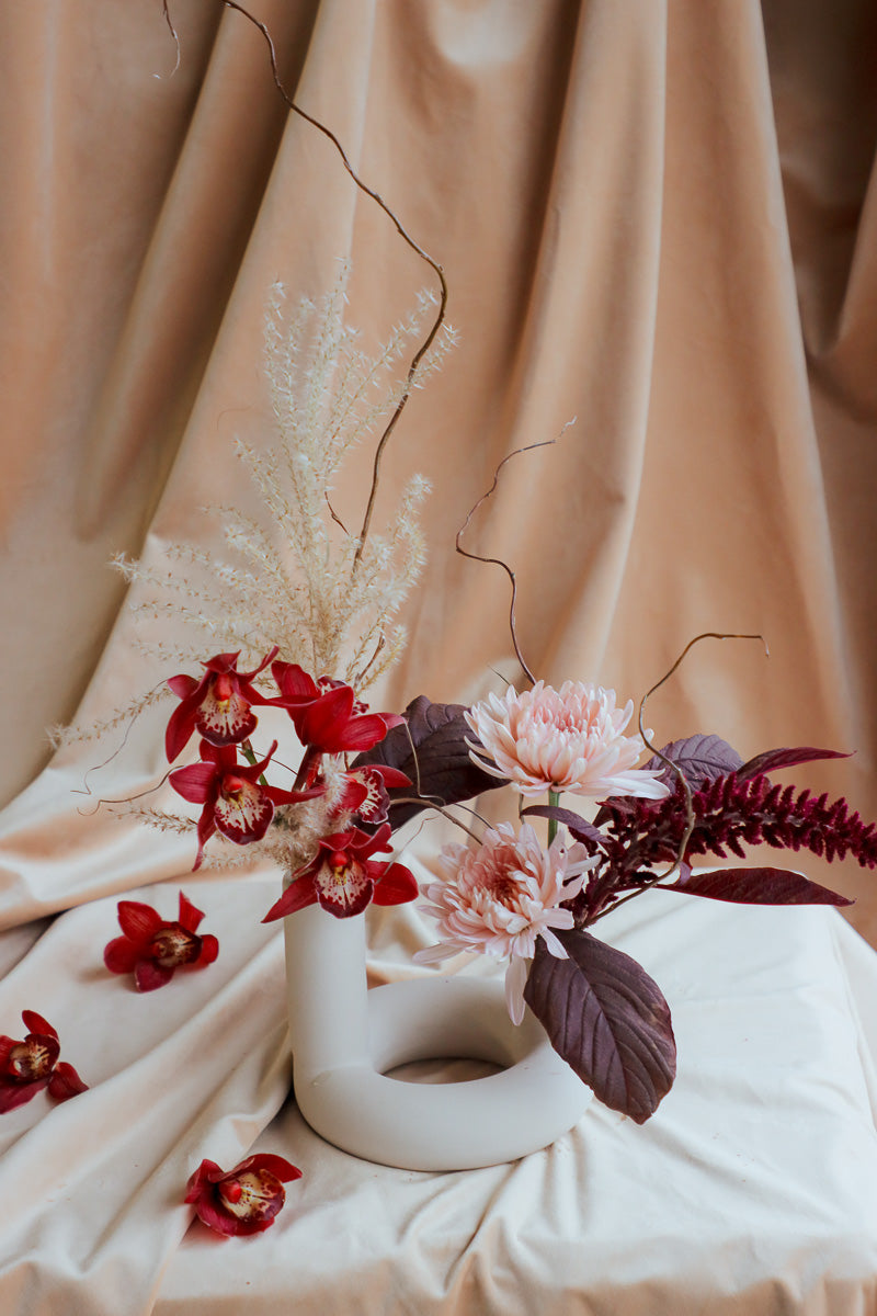 Ember Grace small fall centerpiece in ivory ceramic vase with two openings, featuring burgundy, peach, and ivory flowers.