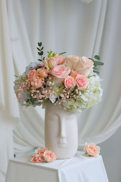 Blush and pastel flower arrangement in white ceramic face vase