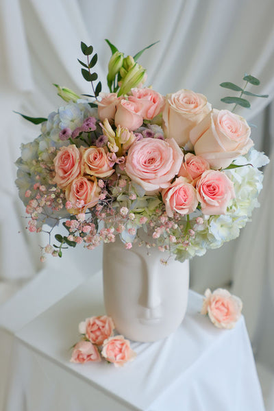 Blush and pastel flower arrangement in white ceramic face vase