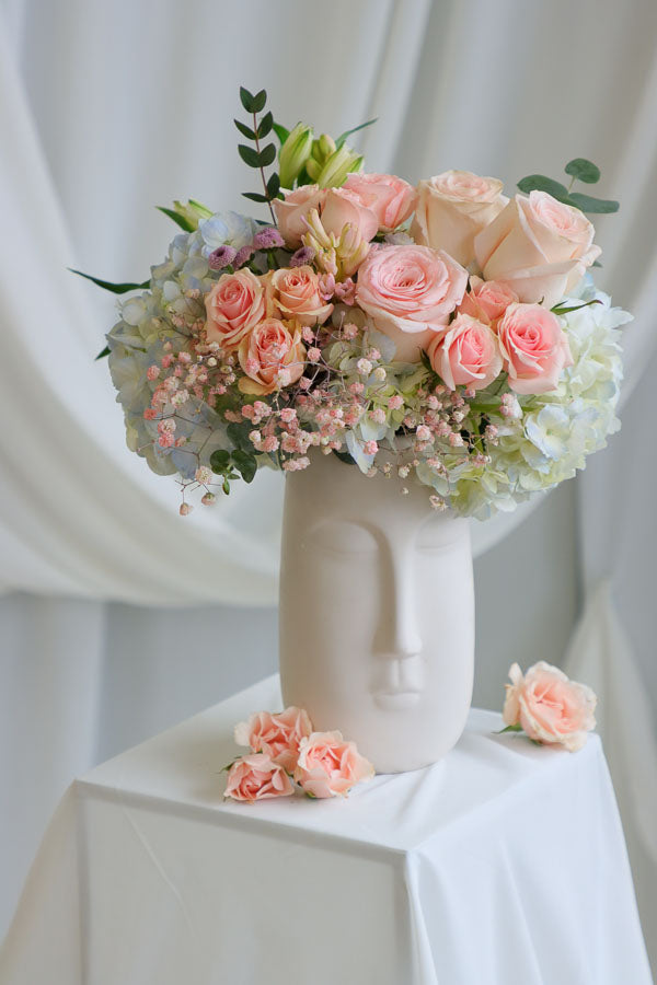 Blush and pastel flower arrangement in white ceramic face vase