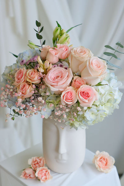 Blush and pastel flower arrangement in white ceramic face vase