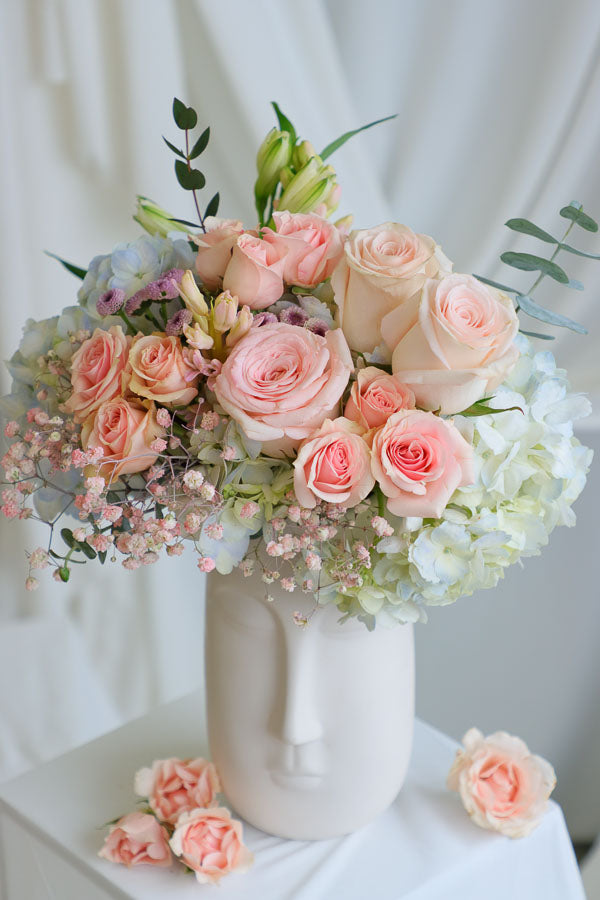 Blush and pastel flower arrangement in white ceramic face vase