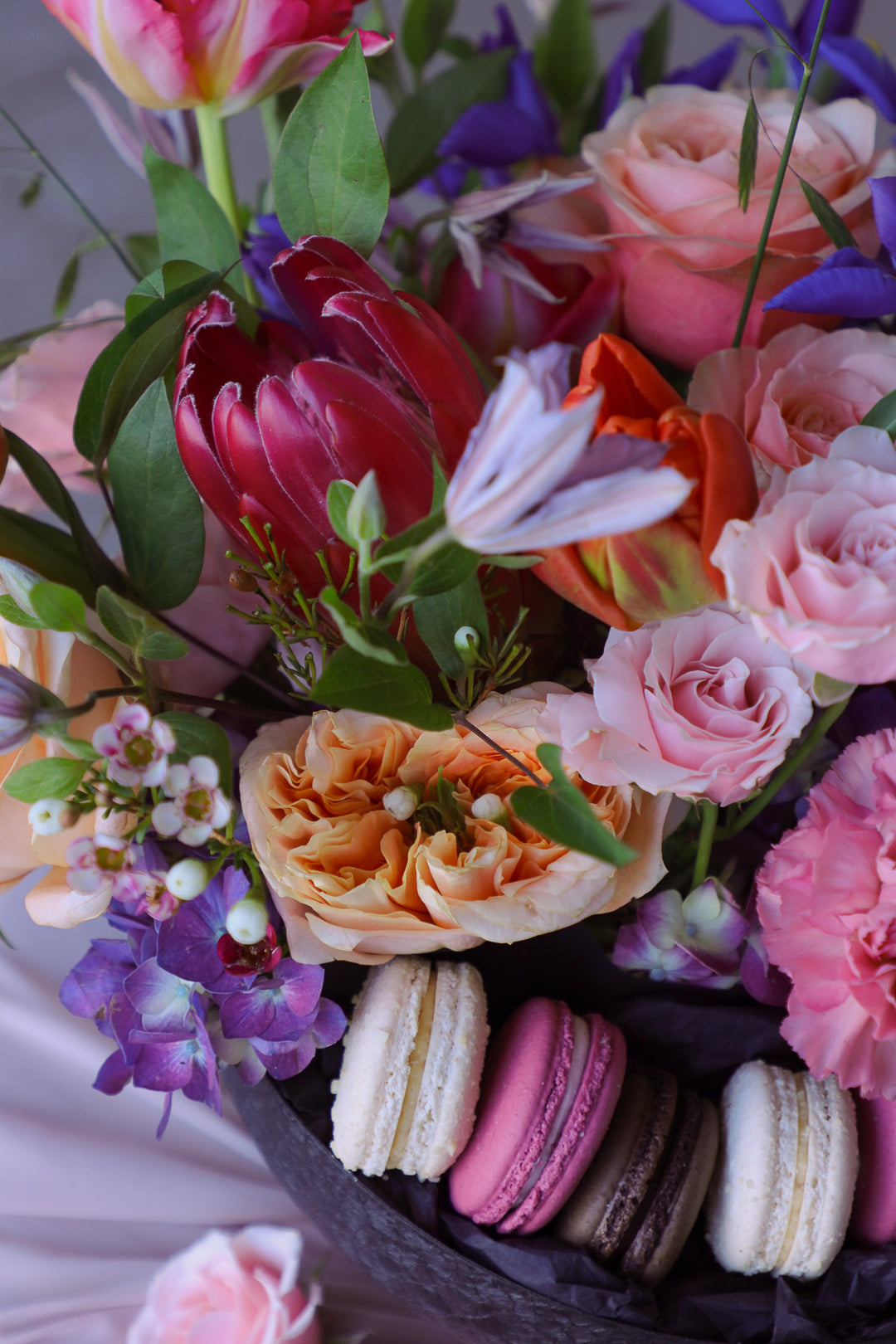 close up of protea, clematis and roses in an artistic summer floral arrangement with macarons styled on a round table.