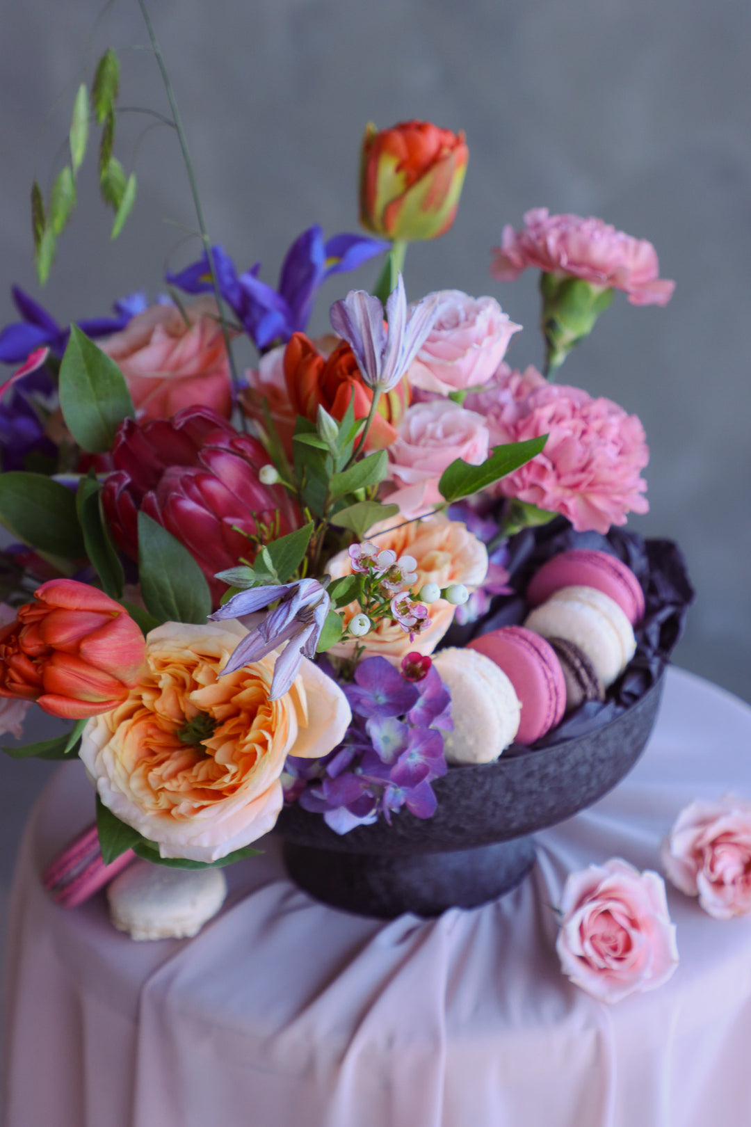 Elevated black compote filled with bright seasonal blooms and delicate macarons.