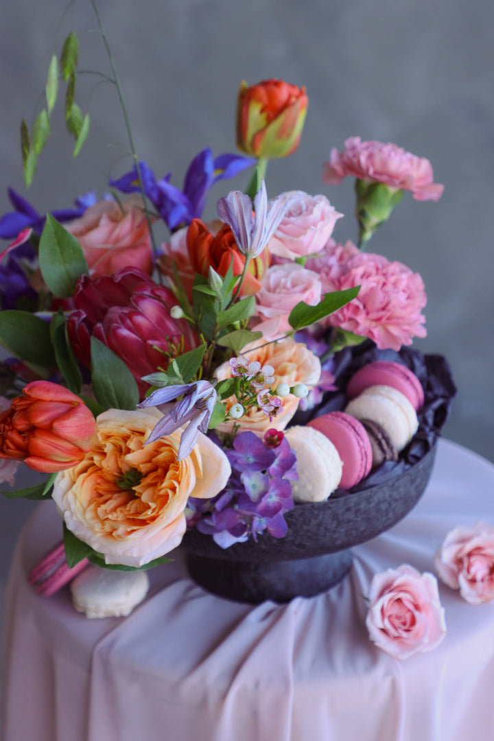 Elevated black compote filled with bright seasonal blooms and delicate macarons.