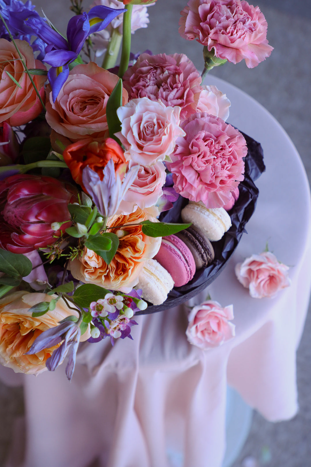 Artistic summer floral arrangement with macarons styled on a round table.