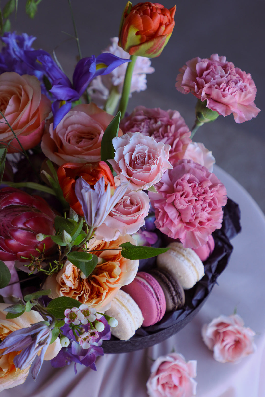Vibrant seasonal flowers and macarons arranged in a black compote