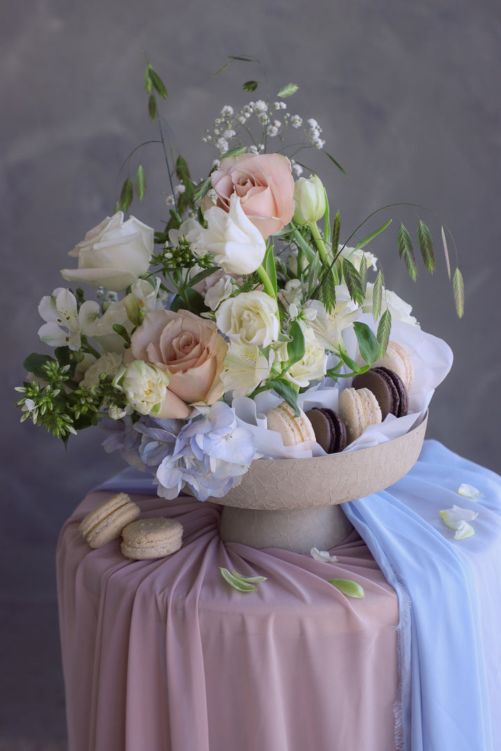 Light and airy flower arrangement in white, blush, and blue with macarons arranged among the flowers.