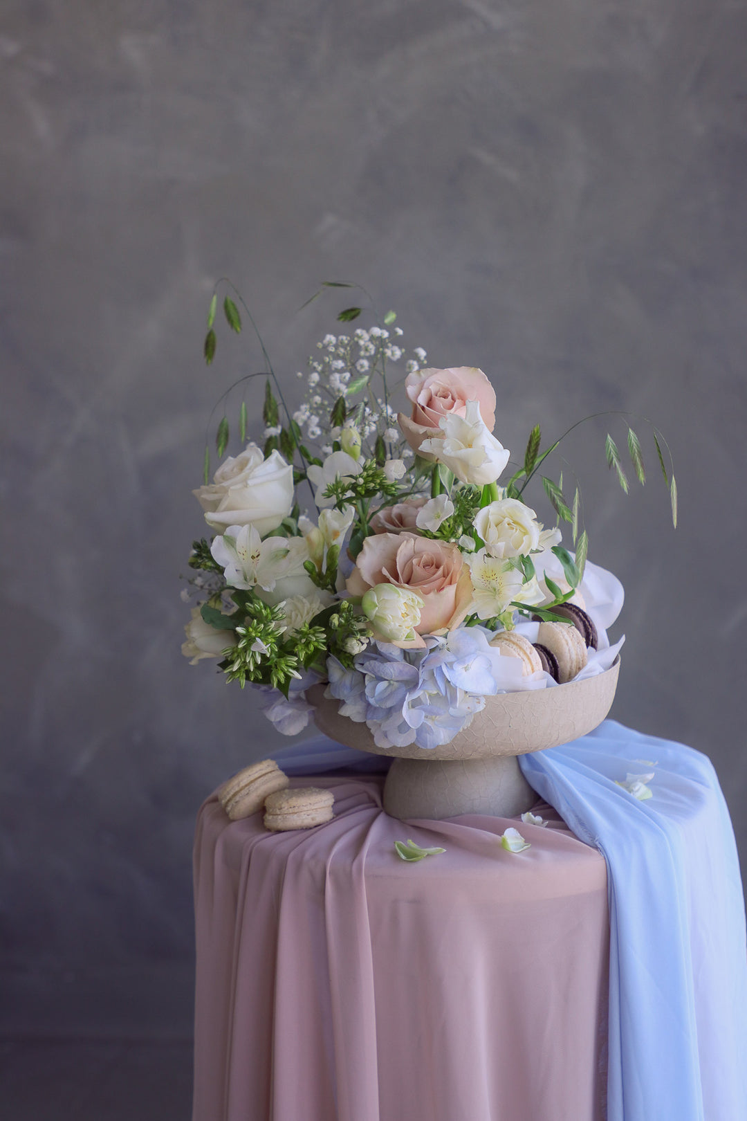 Artistic garden-inspired floral design in a nude pedestal bowl with scattered macarons and flowing fabric.