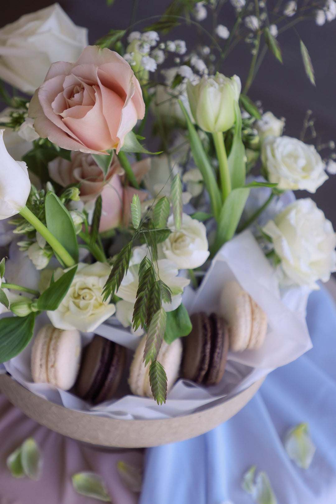 Soft pastel blooms arranged organically in a ceramic pedestal dish with sweet macarons.