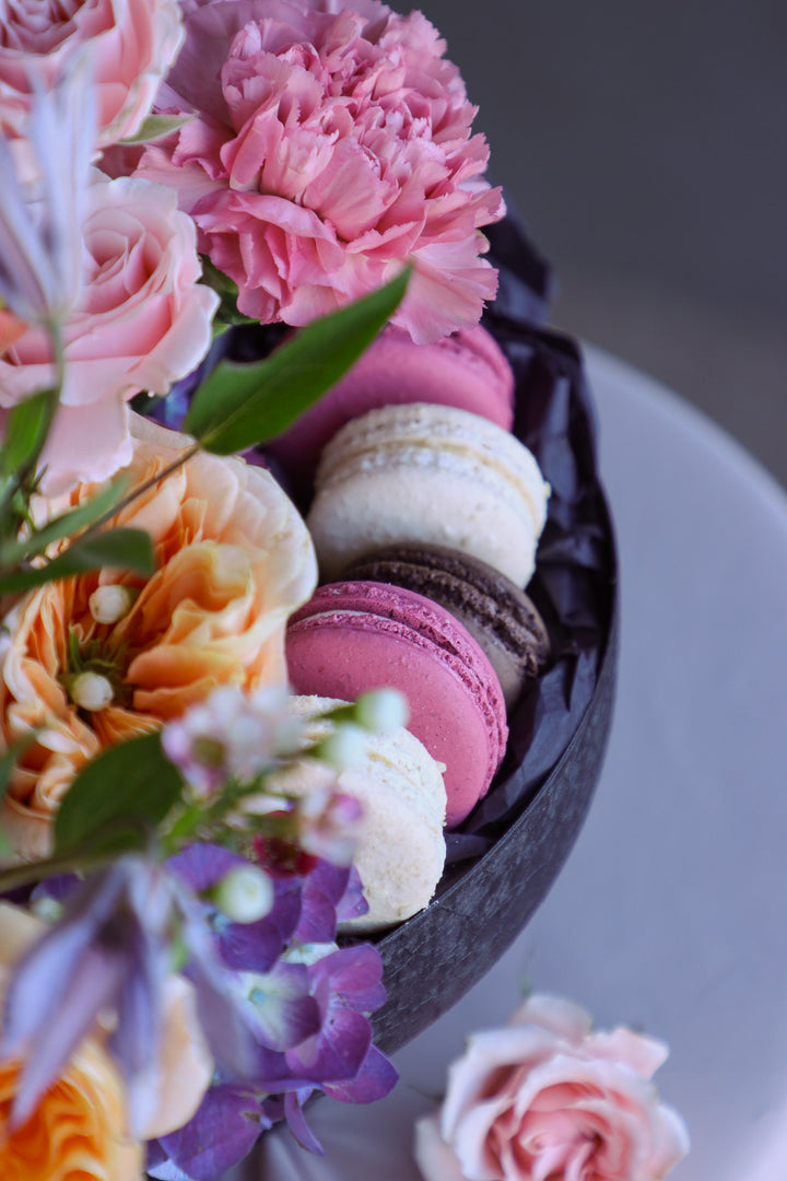 Close up of an elevated black compote filled with bright seasonal blooms and delicate macarons.