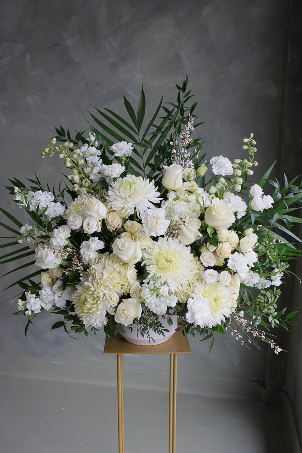 Large white and cream floral arrangement with roses, mums, lisianthus, and greenery in a ceramic vase.
