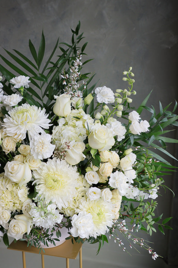 Large white and cream floral arrangement with roses, mums, lisianthus, and greenery in a ceramic vase.