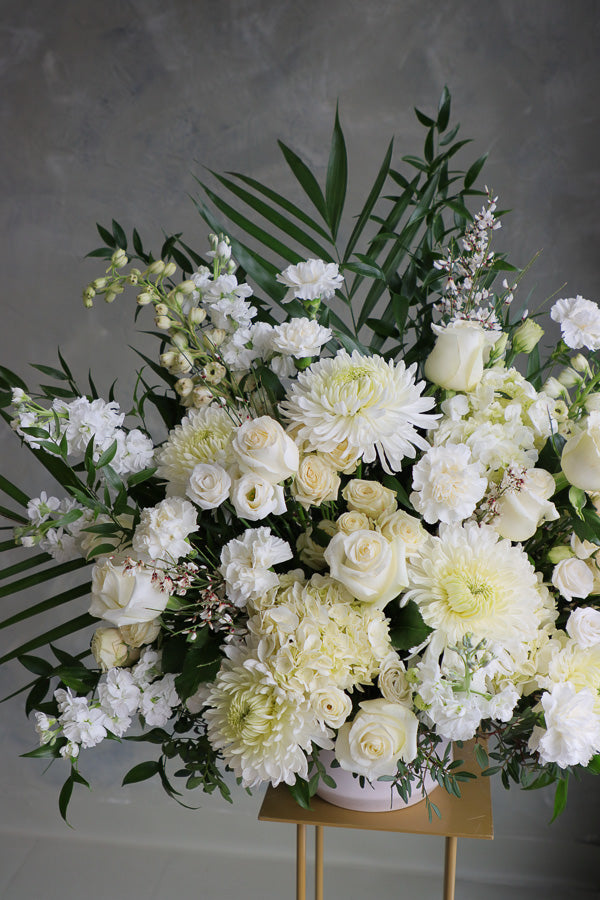 Large white and cream floral arrangement with roses, mums, lisianthus, and greenery in a ceramic vase.
