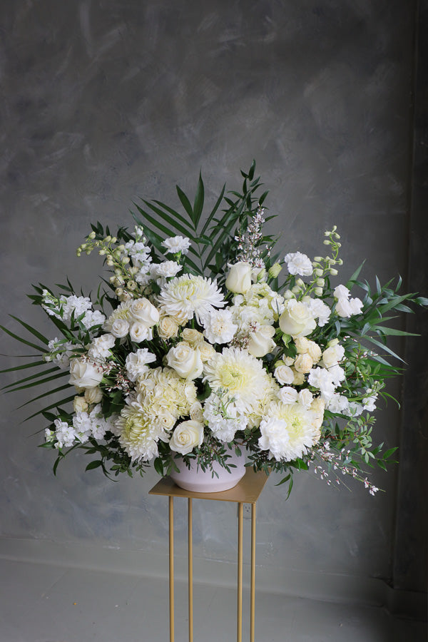 Large white and cream floral arrangement with roses, mums, lisianthus, and greenery in a ceramic vase.