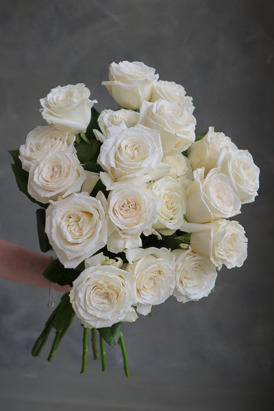Hand holding a single fresh-cut white rose with green leaves, ideal for weddings, sympathy, and floral arrangements