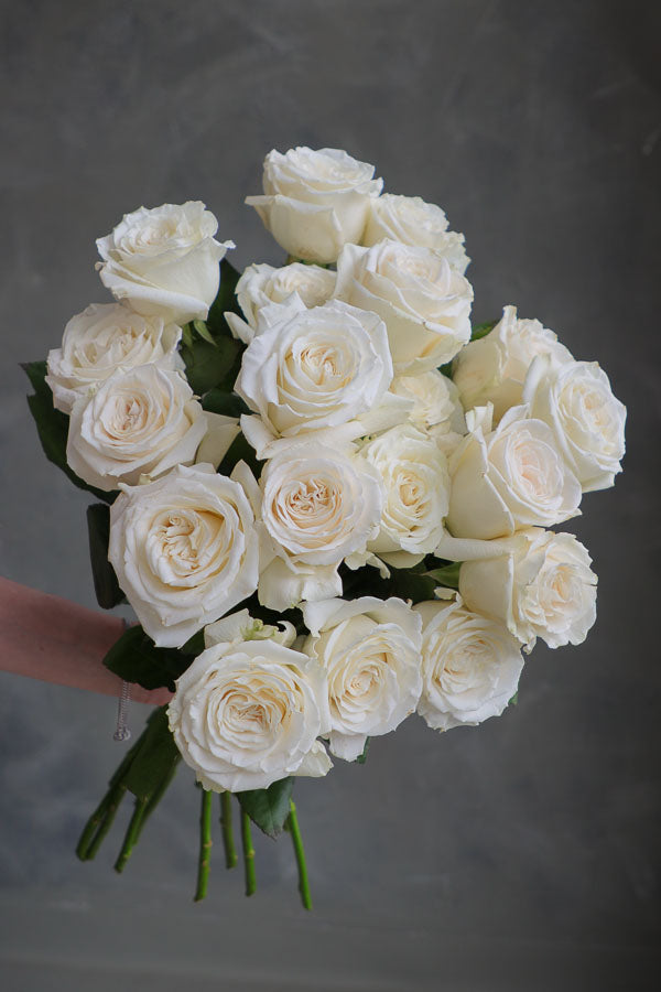 Hand holding a single fresh-cut white rose with green leaves, ideal for weddings, sympathy, and floral arrangements