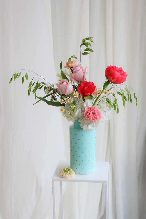 Bright Side flower arrangement with coral peonies, pink roses, blue hydrangeas, and wildflower daisies in a tall blue polka dot vase — cheerful and perfect for any happy occasion.