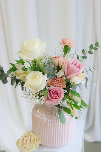 A gentle and delicate floral arrangement featuring blush and white roses with lush white hydrangeas, artfully arranged in an elegant blush ceramic vase. The bouquet exudes warmth, tenderness, and sophistication, perfect for Mother's Day or special occasions.