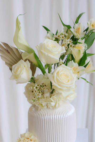 Elegant "Mom's Hug" flower arrangement featuring white and cream roses, hydrangeas, and calla lilies in a stylish cream vase—perfect as Mother's Day flowers or for any heartfelt occasion.