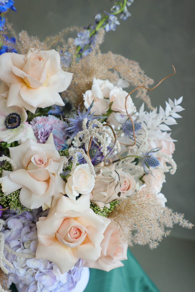 Coastal Dream luxurious floral arrangement with shades of blue, cream, and white, accented by branches and dry decor by Ottawa flower shop.