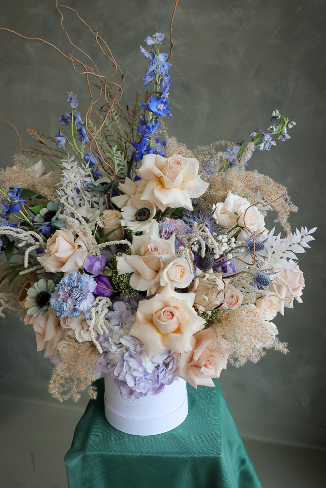 Coastal Dream luxurious floral arrangement with shades of blue, cream, and white, accented by branches and dry decor by Ottawa flower shop.