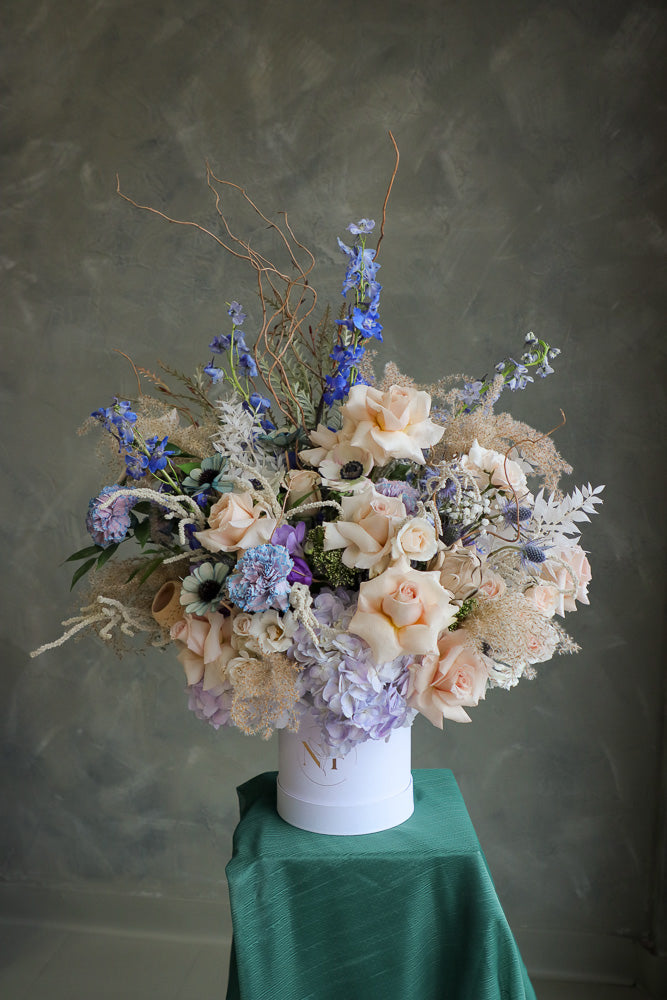 Coastal Dream luxurious floral arrangement with shades of blue, cream, and white, accented by branches and dry decor by Ottawa flower shop.