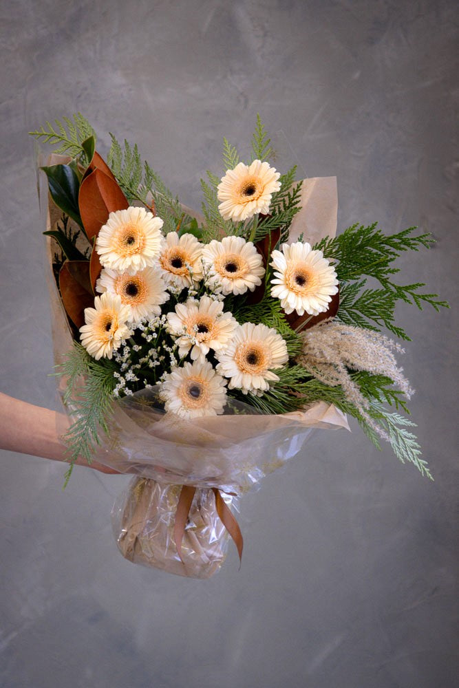 Cozy Winter bouquet with winter foliage, magnolia leaves, dry décor, and peach gerberas wrapped in neutral festive packaging by Ottawa florist.