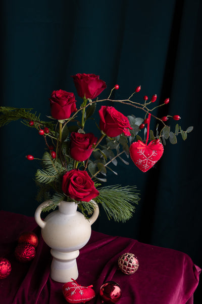 Romantic red roses in ceramic vase with winter greens and heart accent