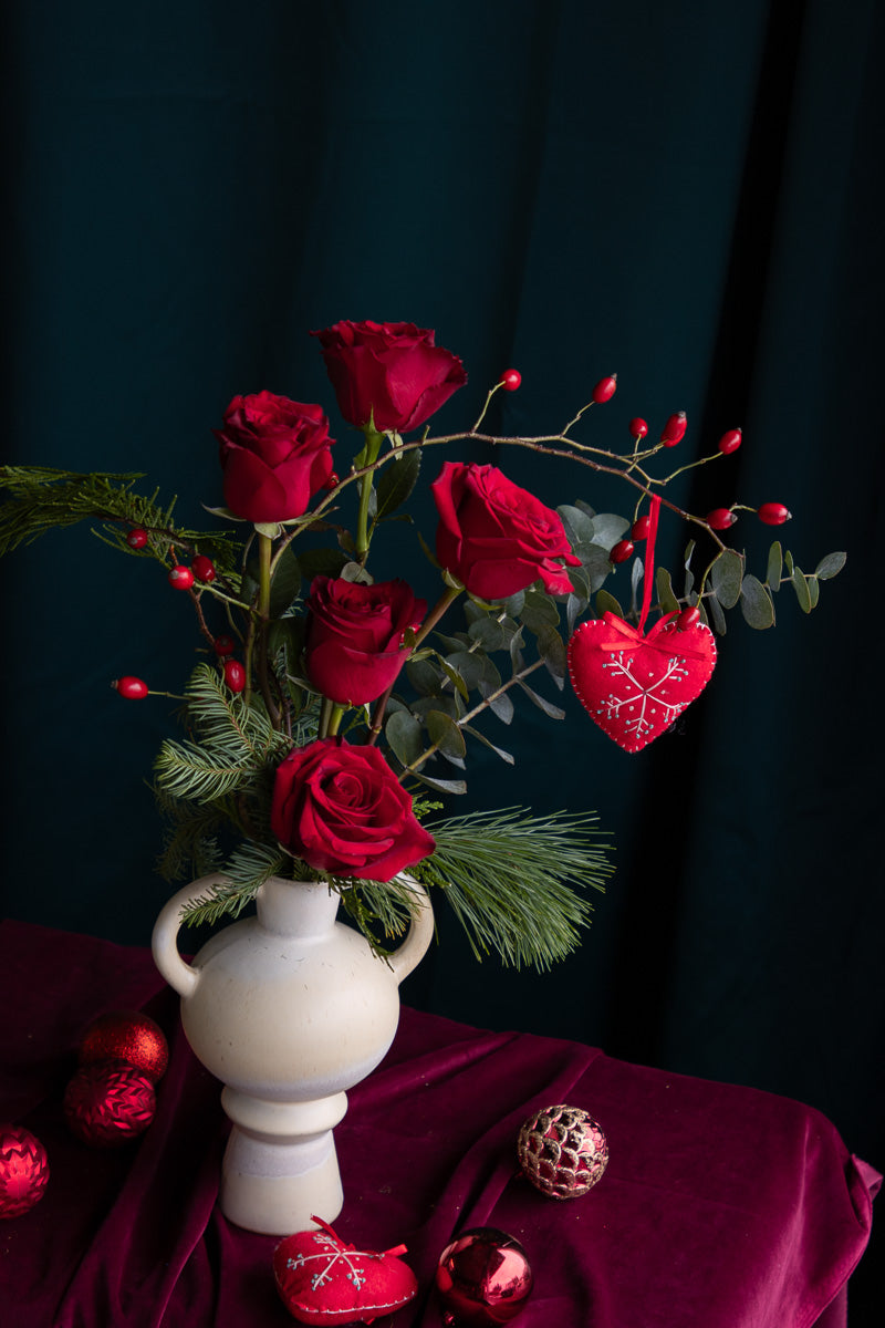 Romantic red roses in ceramic vase with winter greens and heart accent